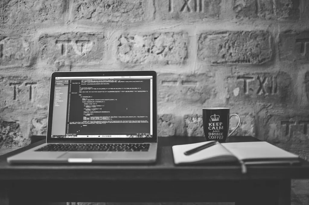 grayscale-photo-of-computer-laptop-near-white-notebook-and-ceramic-mug-on-table-169573 About